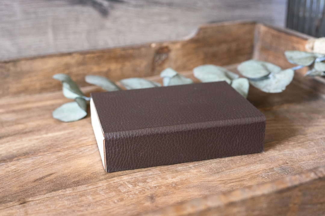 Kleine rechteckige Holzbox für USB‑Stick mit dunkelbraunem Kunstleder‑Umschlag und Magnetverschluss, liegend auf Holztisch – elegante USB‑Geschenkbox